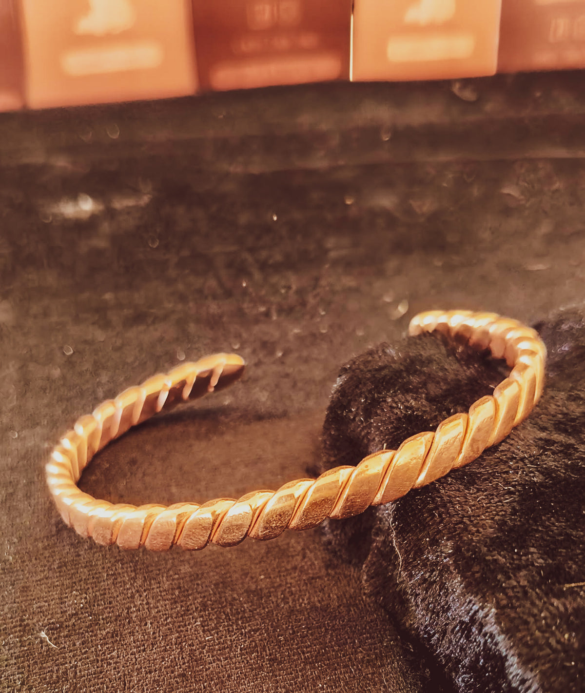 A copper twisted open cuff bracelet displayed on a dark textured surface.
