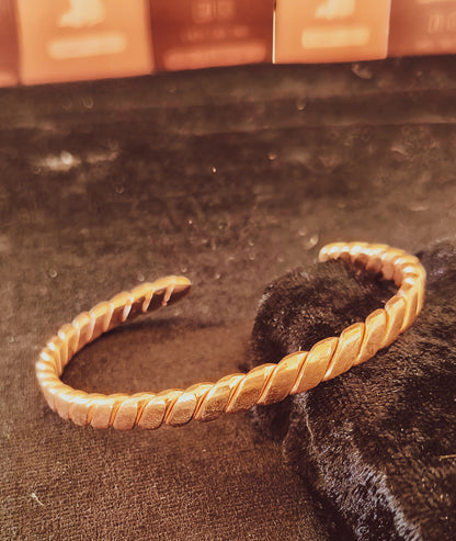 A copper twisted open cuff bracelet displayed on a dark textured surface.